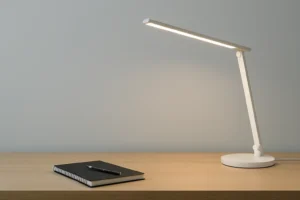 Lámpara de escritorio moderna encendida sobre una mesa de madera con libreta y bolígrafo