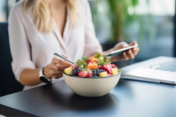 Mujer comiendo un bol de fruta fresca en su escritorio de oficina