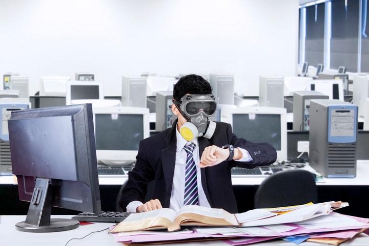 Hombre con mascarilla de gas trabajando en una oficina con muchos ordenadores