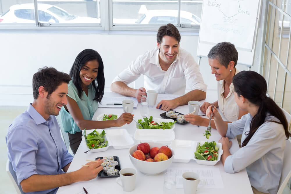 Empleados compartiendo comida saludable en un comedor de oficina con luz natural