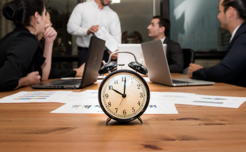 Reloj sobre mesa con equipo de trabajo desenfocado al fondo
